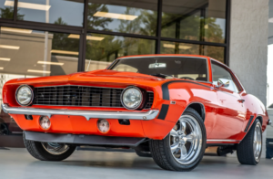 a classic orange car is parked in front of glass windows